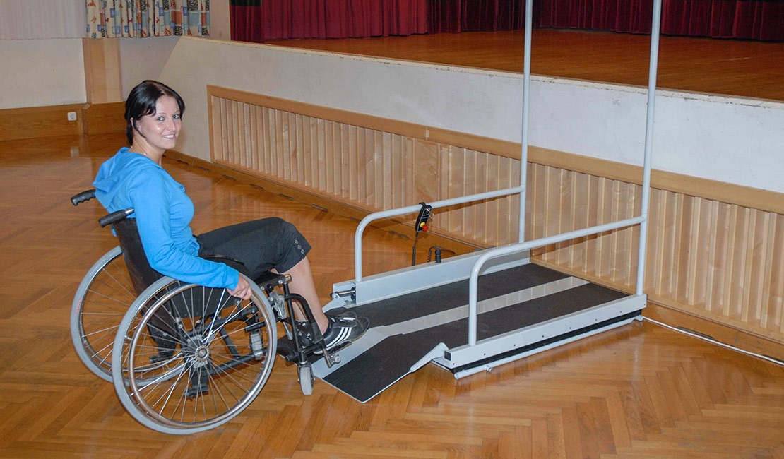 Eine junge Dame benutzt mit ihrem Rollstuhl den LIFTBOY, um die Bühne zu erreichen