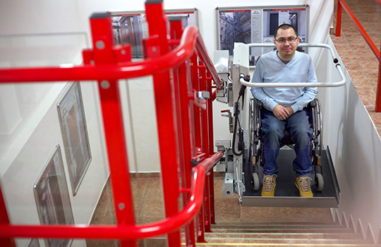 Ein junger Herr benutzt mit seinem Rollstuhl den Plattformtreppenlift STRATOS im Innenbereich